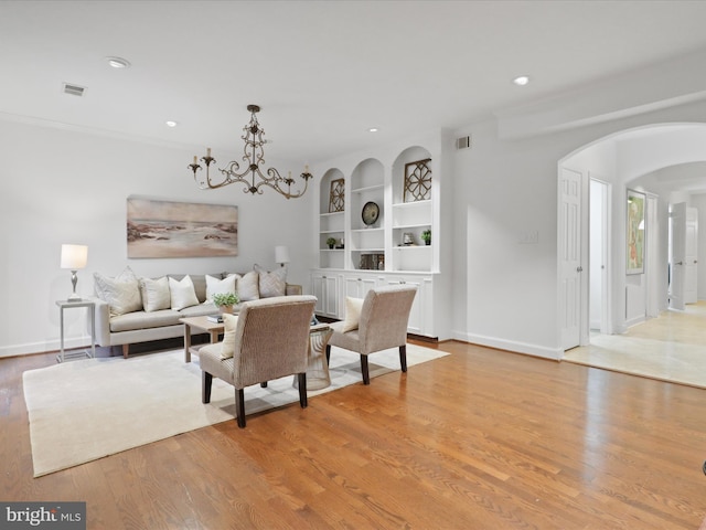 living room featuring arched walkways, recessed lighting, light wood-style flooring, and built in shelves