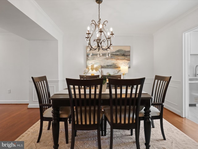 dining room with a decorative wall, a notable chandelier, wood finished floors, and ornamental molding