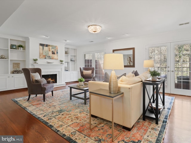 living room with french doors, a lit fireplace, visible vents, and wood finished floors