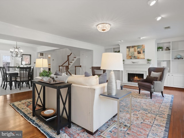 living room with stairway, wood finished floors, visible vents, a premium fireplace, and an inviting chandelier