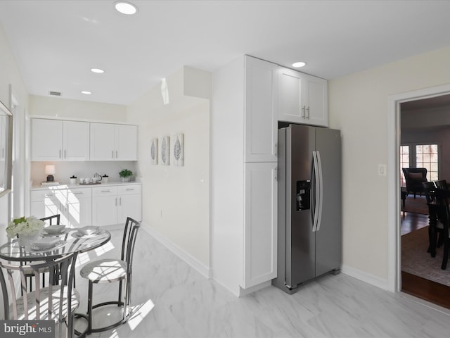 kitchen featuring baseboards, recessed lighting, stainless steel refrigerator with ice dispenser, marble finish floor, and white cabinetry