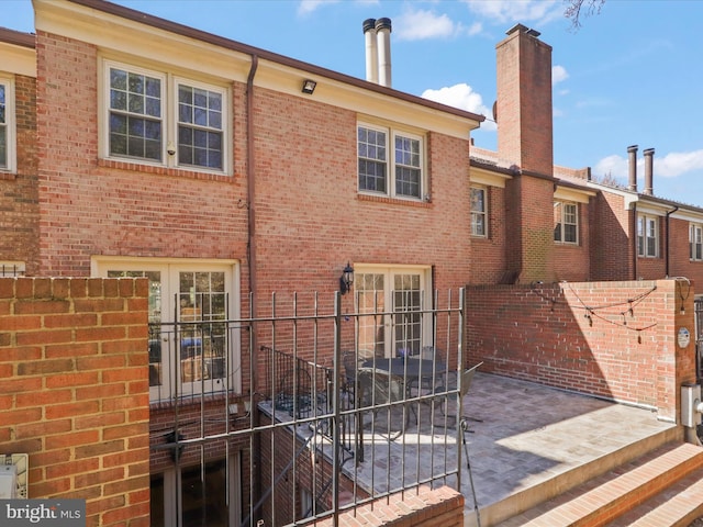 rear view of house with brick siding, a patio area, a chimney, and fence