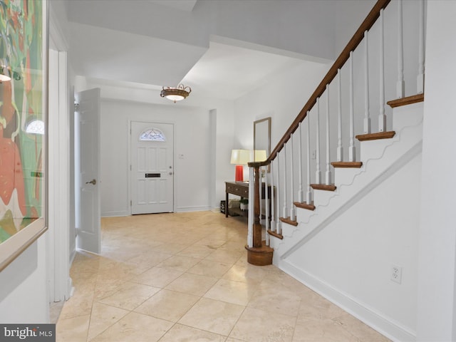 foyer entrance with light tile patterned flooring, stairs, and baseboards