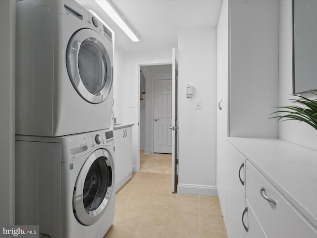 laundry room featuring light tile patterned floors, cabinet space, stacked washer and clothes dryer, and baseboards