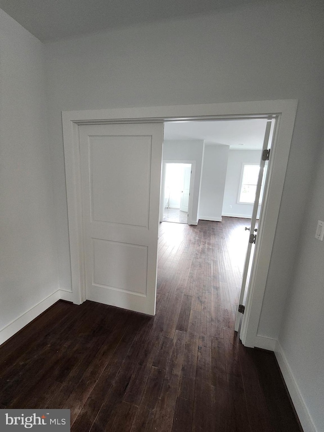 corridor with dark wood-type flooring and baseboards
