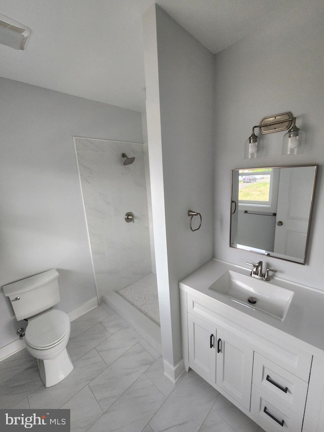 bathroom with a tile shower, toilet, marble finish floor, and vanity