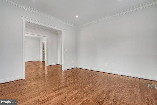 empty room featuring crown molding, visible vents, light wood-style flooring, and baseboards