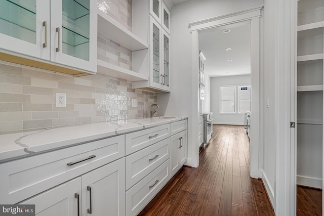 kitchen with white cabinets, a sink, dark wood-style floors, light stone countertops, and decorative backsplash