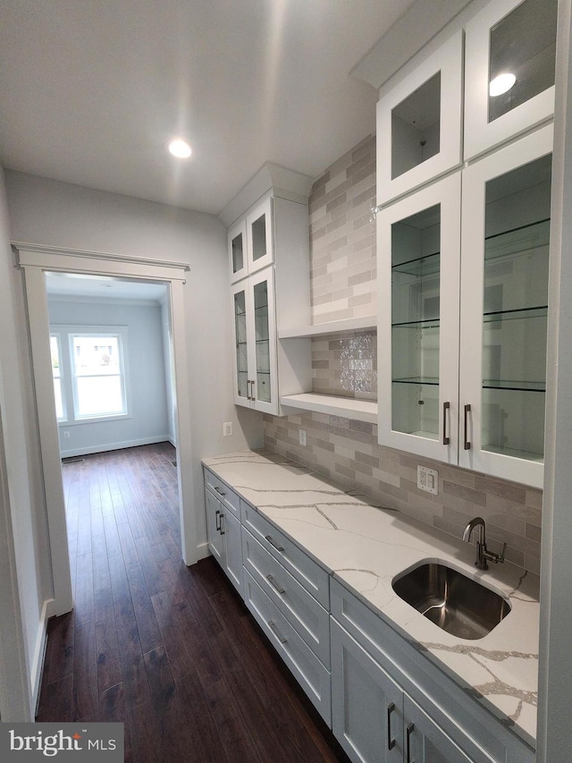 kitchen with dark wood-style floors, backsplash, white cabinets, light stone countertops, and a sink