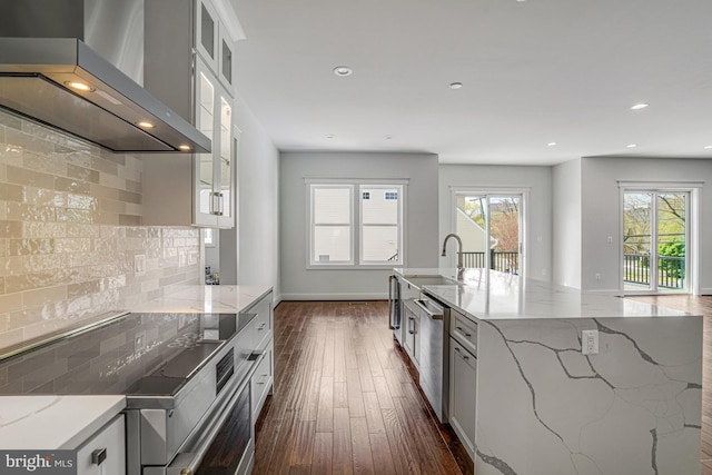 kitchen with dark wood-style flooring, wall chimney range hood, dishwasher, and light stone countertops