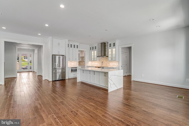 kitchen featuring light countertops, stainless steel refrigerator with ice dispenser, visible vents, wall chimney exhaust hood, and a sink