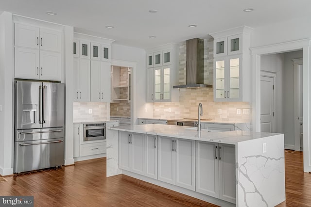 kitchen with wall chimney exhaust hood, dark wood finished floors, white cabinets, a center island with sink, and high end fridge
