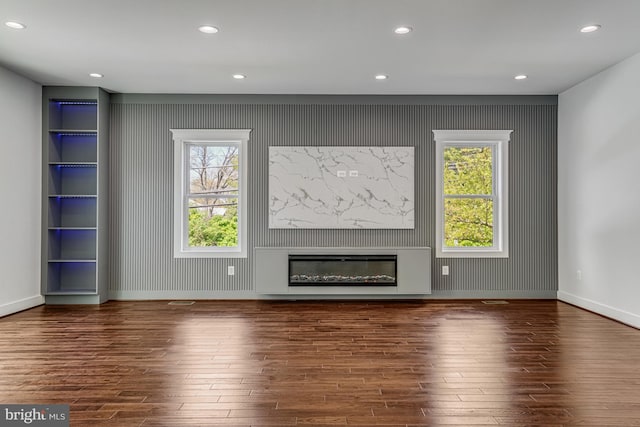 unfurnished living room featuring wood finished floors, baseboards, a glass covered fireplace, and recessed lighting