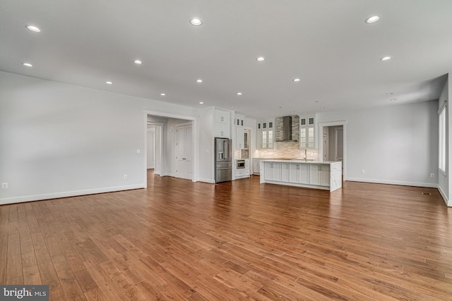 unfurnished living room with recessed lighting, a sink, light wood-type flooring, and baseboards