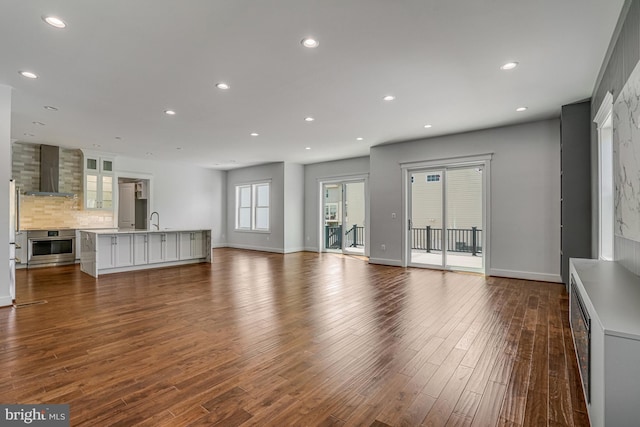 unfurnished living room featuring a sink, baseboards, recessed lighting, and dark wood-style floors