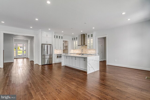kitchen with tasteful backsplash, white cabinets, wall chimney exhaust hood, high quality fridge, and dark wood-style floors