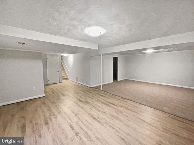 finished basement featuring visible vents, baseboards, stairs, wood finished floors, and a textured ceiling