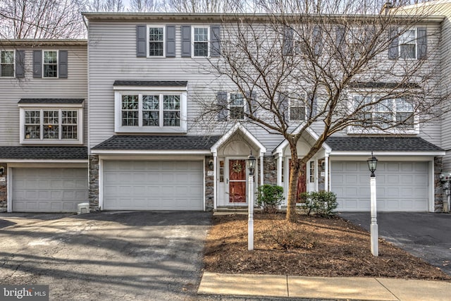 townhome / multi-family property with an attached garage, stone siding, driveway, and a shingled roof