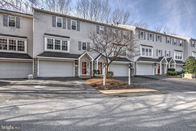 multi unit property featuring stone siding, driveway, and an attached garage