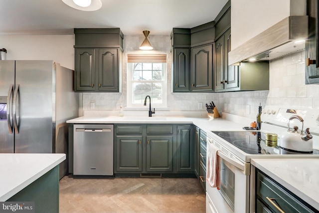 kitchen with tasteful backsplash, wall chimney range hood, light countertops, stainless steel appliances, and a sink