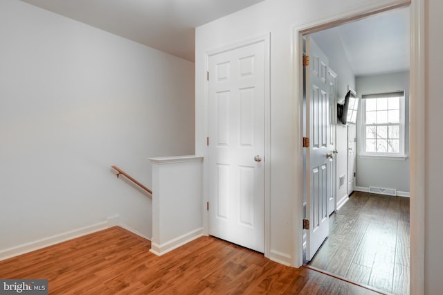 corridor with an upstairs landing, visible vents, baseboards, and wood finished floors