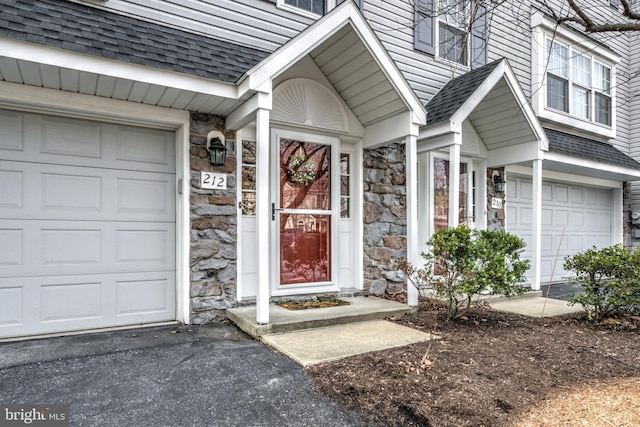 doorway to property with stone siding, driveway, and a shingled roof