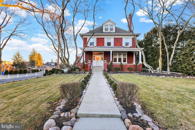 view of front of house featuring brick siding, covered porch, a front yard, and fence