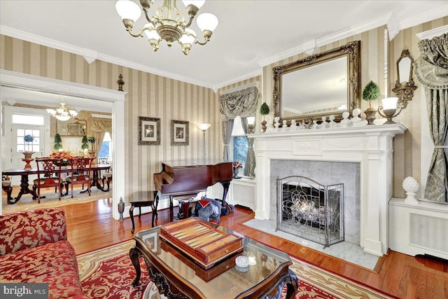 living area with a high end fireplace, wallpapered walls, crown molding, an inviting chandelier, and wood finished floors