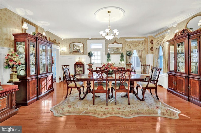 dining space featuring wallpapered walls, ornamental molding, wainscoting, an inviting chandelier, and wood finished floors