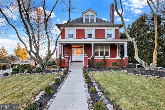 american foursquare style home featuring brick siding, a porch, and a front lawn