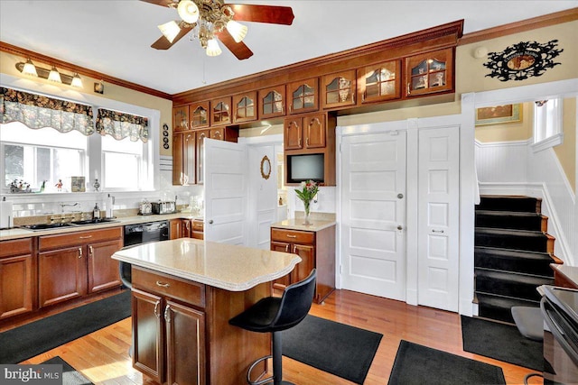 kitchen with brown cabinets, a sink, light wood finished floors, ceiling fan, and light countertops