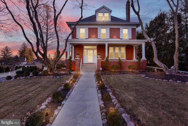 american foursquare style home featuring brick siding, a porch, and fence