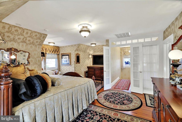 bedroom with wallpapered walls, wood finished floors, french doors, and visible vents