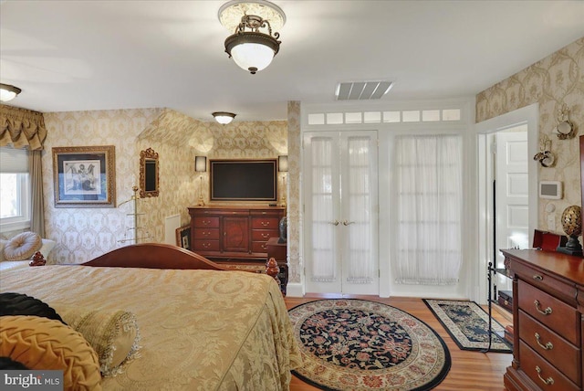 bedroom with visible vents, wood finished floors, and wallpapered walls