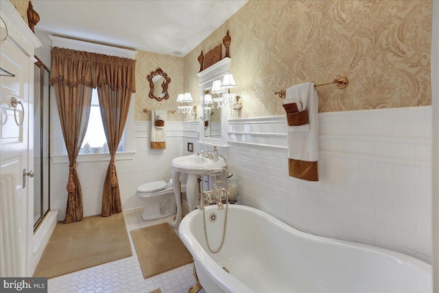 bathroom featuring a wainscoted wall, toilet, a shower stall, wallpapered walls, and a freestanding bath