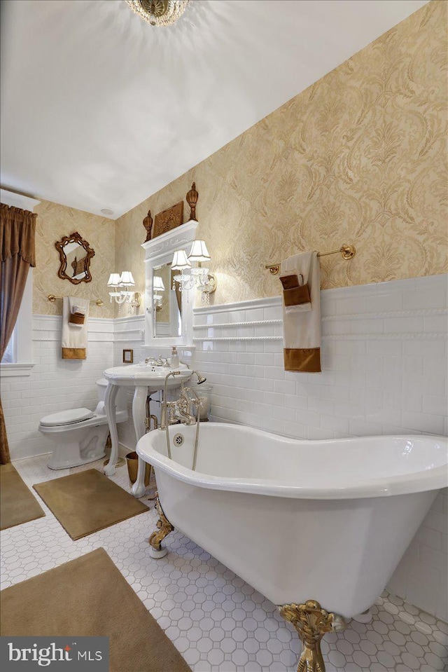 full bath with wainscoting, toilet, wallpapered walls, and a freestanding tub