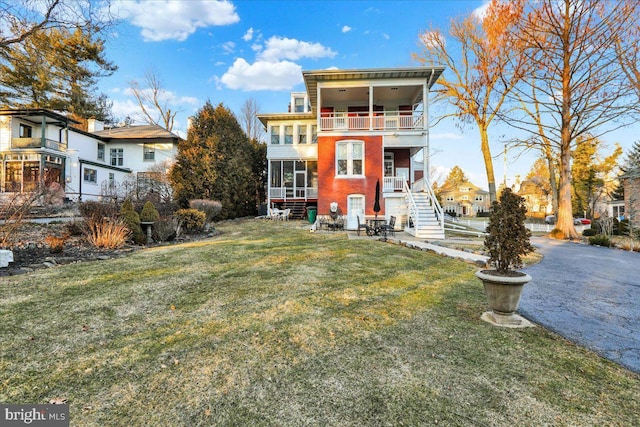 rear view of house featuring a lawn, stairs, a balcony, and a sunroom