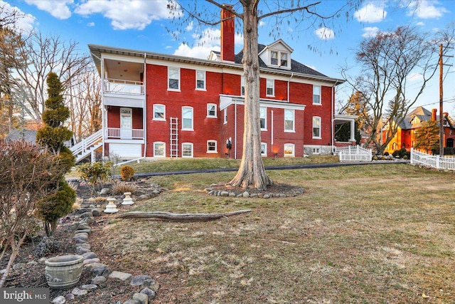 back of property with a balcony, a lawn, brick siding, and a chimney