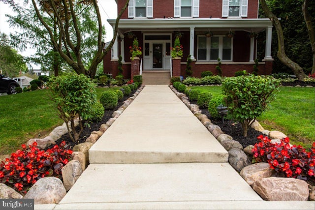 doorway to property with a porch, a lawn, and brick siding