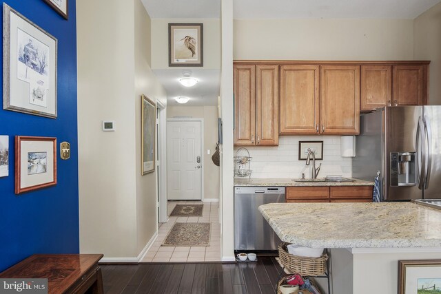 kitchen featuring tasteful backsplash, light stone countertops, appliances with stainless steel finishes, brown cabinetry, and a sink