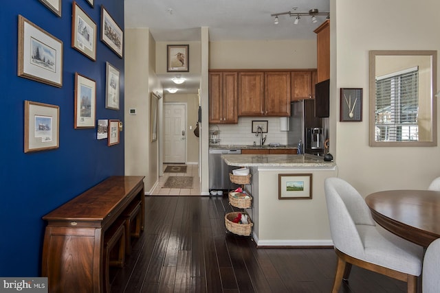 kitchen featuring dark wood-type flooring, a sink, tasteful backsplash, appliances with stainless steel finishes, and brown cabinetry