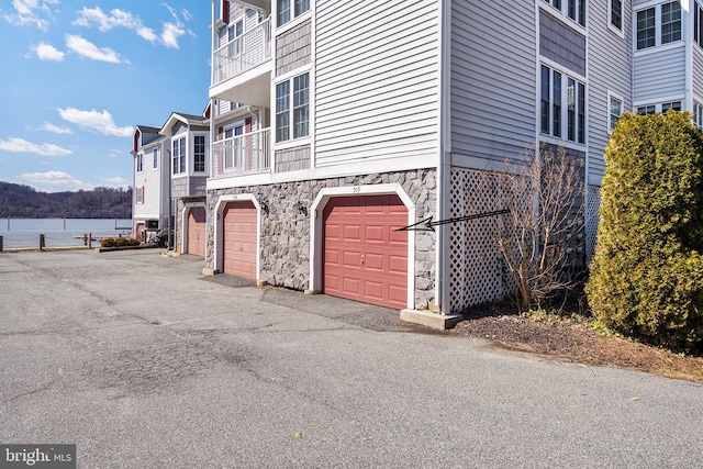 view of home's exterior with stone siding, an attached garage, and a water view