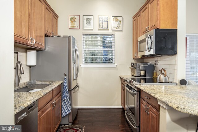 kitchen with a sink, appliances with stainless steel finishes, brown cabinetry, baseboards, and dark wood-style flooring