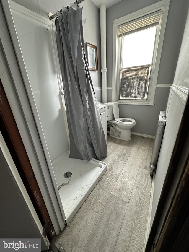 bathroom with toilet, wood finished floors, and a stall shower