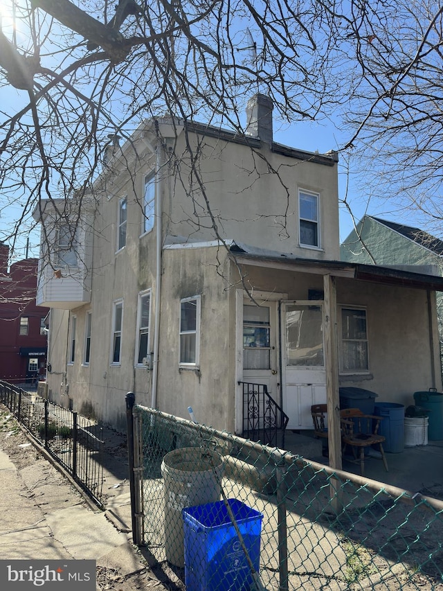 view of side of property with a fenced front yard, stucco siding, a chimney, a patio area, and a gate