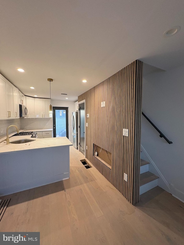 kitchen with light countertops, light wood-type flooring, appliances with stainless steel finishes, white cabinets, and a sink