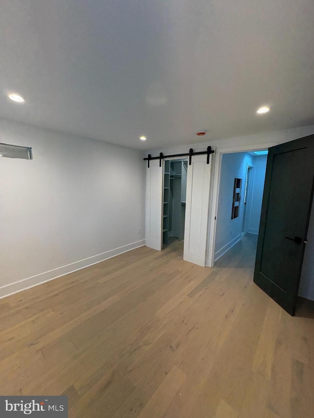 spare room featuring recessed lighting, baseboards, light wood-type flooring, and a barn door