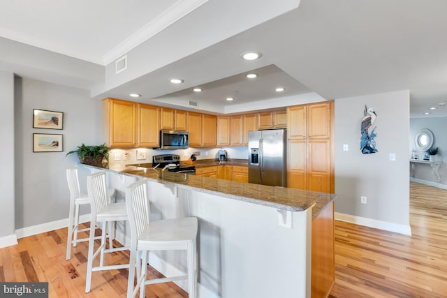 kitchen with visible vents, light wood finished floors, a peninsula, appliances with stainless steel finishes, and a kitchen bar