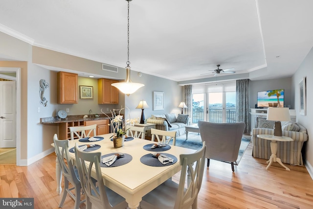 dining space with visible vents, a ceiling fan, light wood-style floors, crown molding, and baseboards