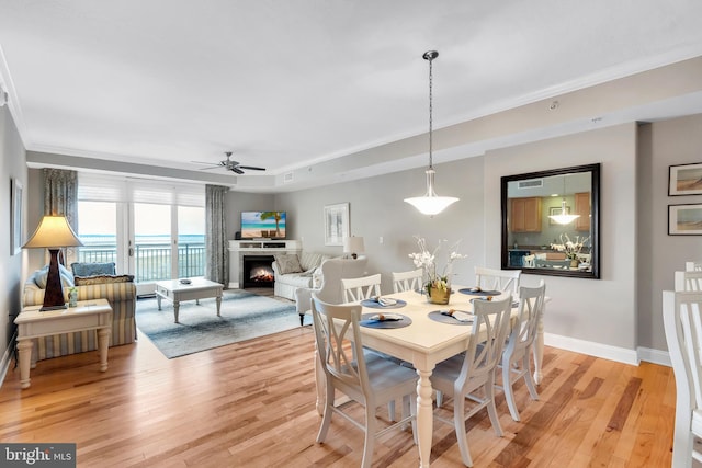 dining area with ceiling fan, a warm lit fireplace, light wood-type flooring, and baseboards